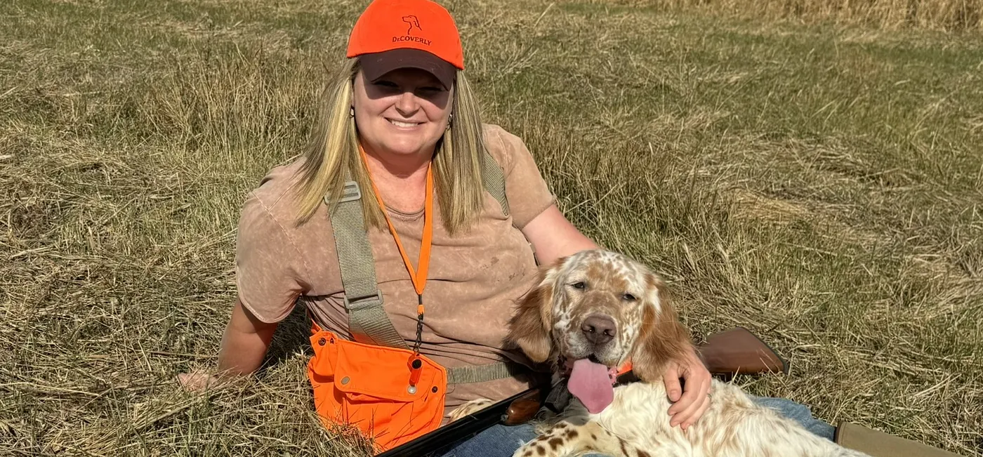 Courtney sitting in a broomsedge field with an orange belton setter beside her